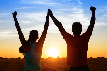 21976515 - successful couple of young athletes raising arms to golden summer sunset sky after training fitness man and woman with arms up celebrating sport goals after exercising in countryside field