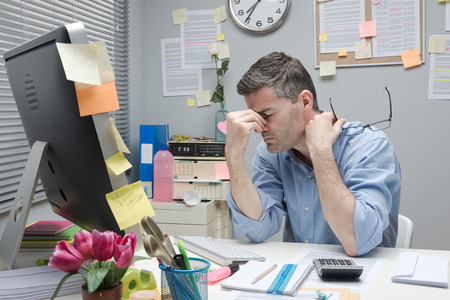 33304135 - depressed bored office worker at his desk holding glasses.